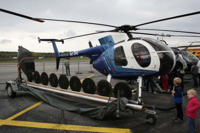 Helikopter, Hughes 369D, SE-JPE från HeliAir Sweden och  framför den röjsåg som kan hängs under helikoptern för att bl.a. röja intill kraftledningsgator. Foto: Hans Groby.