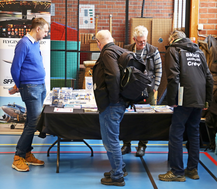 Robert Malmstedt från SFF Stockholm informerar ett par besökare om Svensk Flyghistorisk Förenings verksamhet i SFF:s monter. Foto: Gunnar Åkerberg.