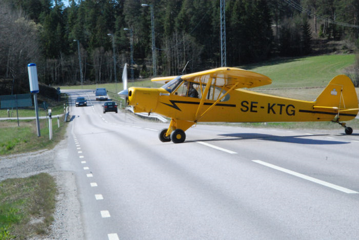 En Piper PA-18-150 Super Cub taxar över bilvägen för att komma till uppställningsplatsen vid flygfältet i Vallentuna. Foto: Bengt Simson.