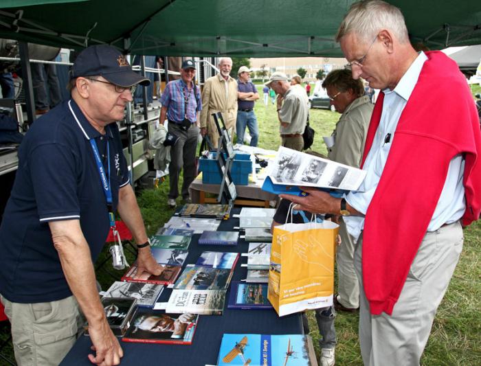 Utrikesminister Carl Bildt besökte SFF:s utställning på flygfestivalen under lördagen. Här bläddrar han intresserat i Sven Stridsbergs Blériot-häfte medan Bernt Olsson från SFF Stockholm tipsar om lite avkopplande läsning inför den kommande valrörelsen… Till slut föll valet på SFF:s flyghistoriska revy om System 37 Viggen som inhandlades innan utrikesministern skyndade vidare. Foto: Gunnar Åkerberg.